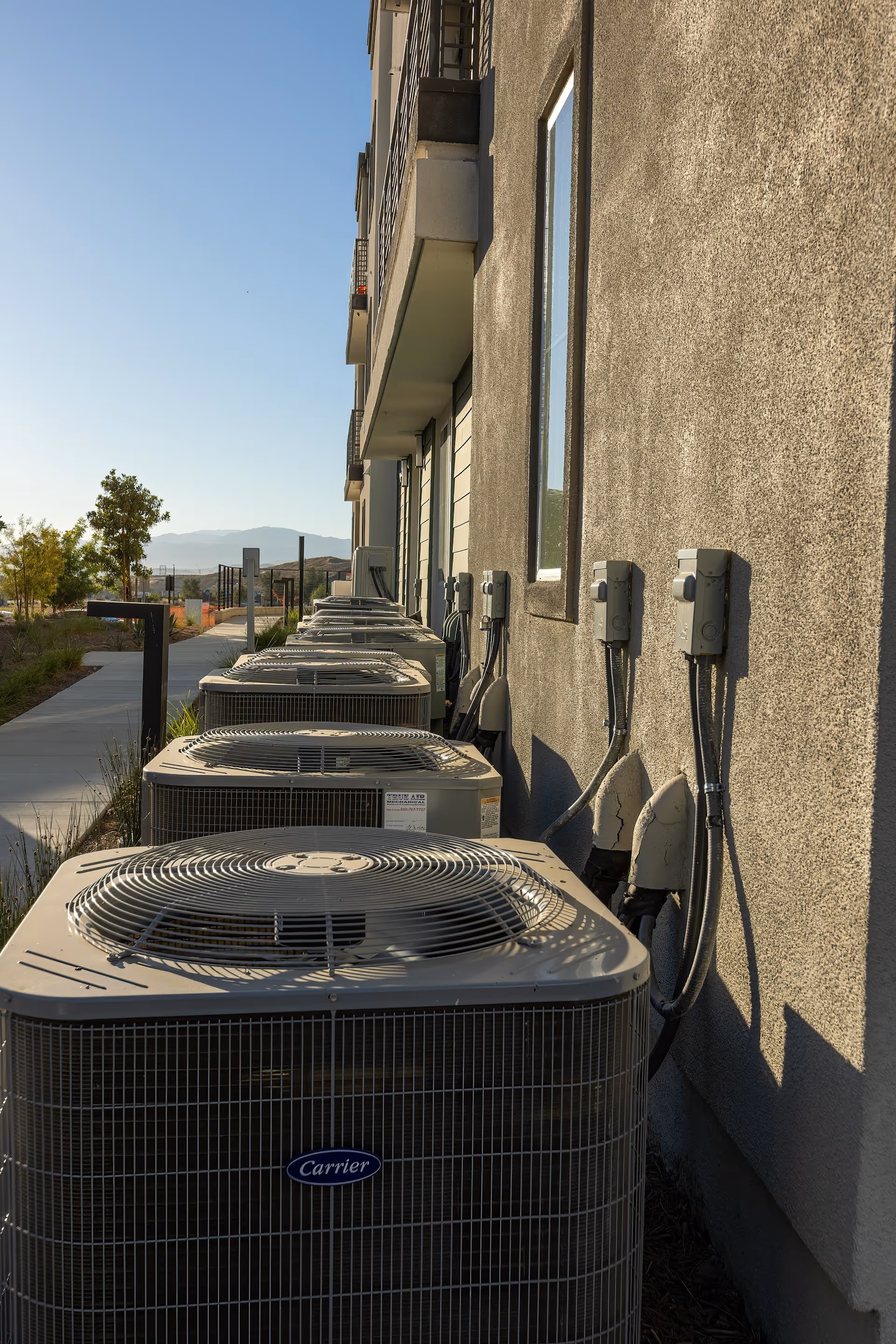 Row of Carrier brand air conditioning units lined up outside a building with electrical boxes mounted on the wall.