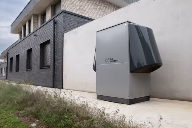 Modern heat pump unit installed outside a brick and white wall building.