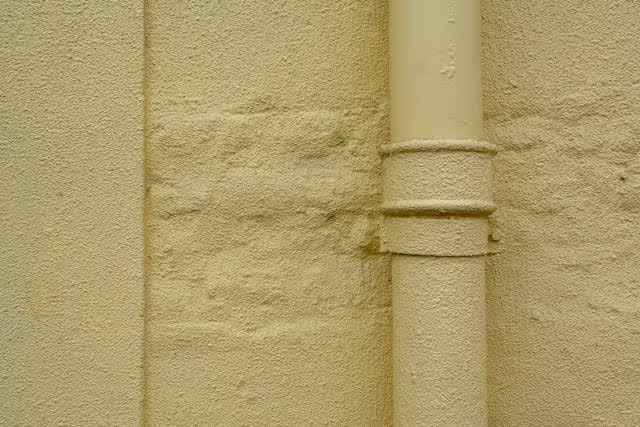 Close-up of a beige textured wall with a vertical beige pipe attached.